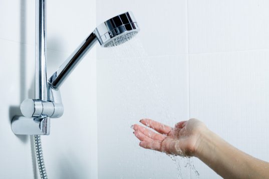 Wie viel Liter passen in eine Badewanne? So viel Wasser benötigen Sie! 14 Frau hält Hand unter Duschbrause