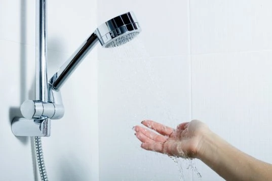Wie viel Liter passen in eine Badewanne? So viel Wasser benötigen Sie! 14 Frau hält Hand unter Duschbrause